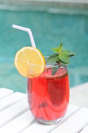 Glass of delicious cocktail on white wooden table near swimming pool. Refreshing drink