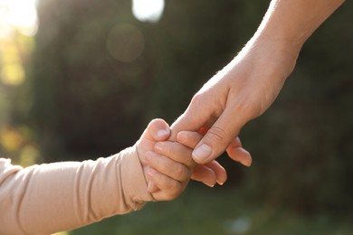 Daughter holding mother's hand outdoors, closeup view