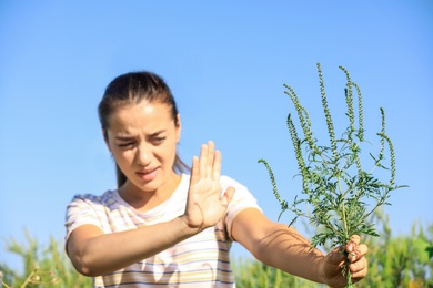 Young woman with ragweed branch suffering from allergy outdoors, focus on hand