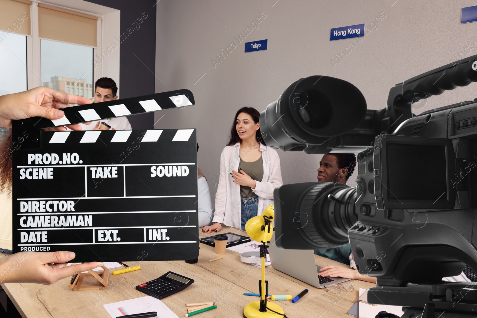 Image of Shooting movie. Second assistant camera holding clapperboard near video camera in front of coworkers (actors) at office (film set)