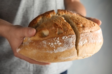 Man holding whole wheat bread on grey background, closeup