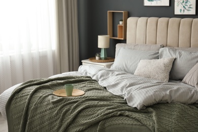 Photo of Comfortable bed with knitted green plaid in stylish room interior