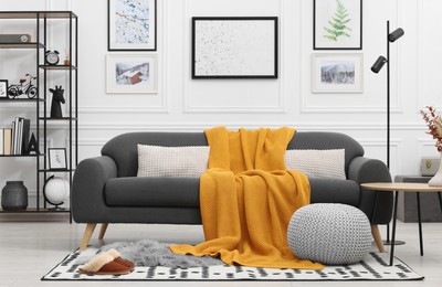 Photo of Stylish living room interior with comfortable sofa, blanket, side table and ottoman
