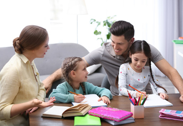 Photo of Parents helping their daughters with homework at table indoors