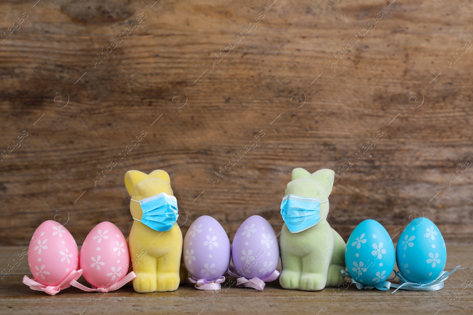 Image of COVID-19 pandemic. Easter bunnies in protective mask and colorful eggs on wooden background