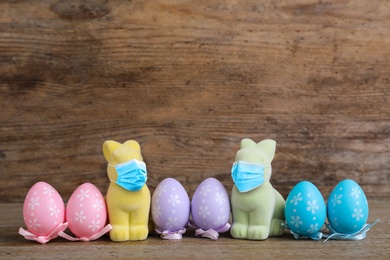 COVID-19 pandemic. Easter bunnies in protective mask and colorful eggs on wooden background