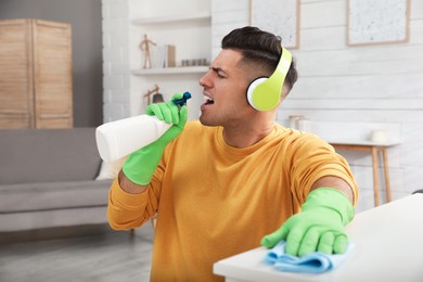 Photo of Man with spray bottle and rag singing while cleaning at home