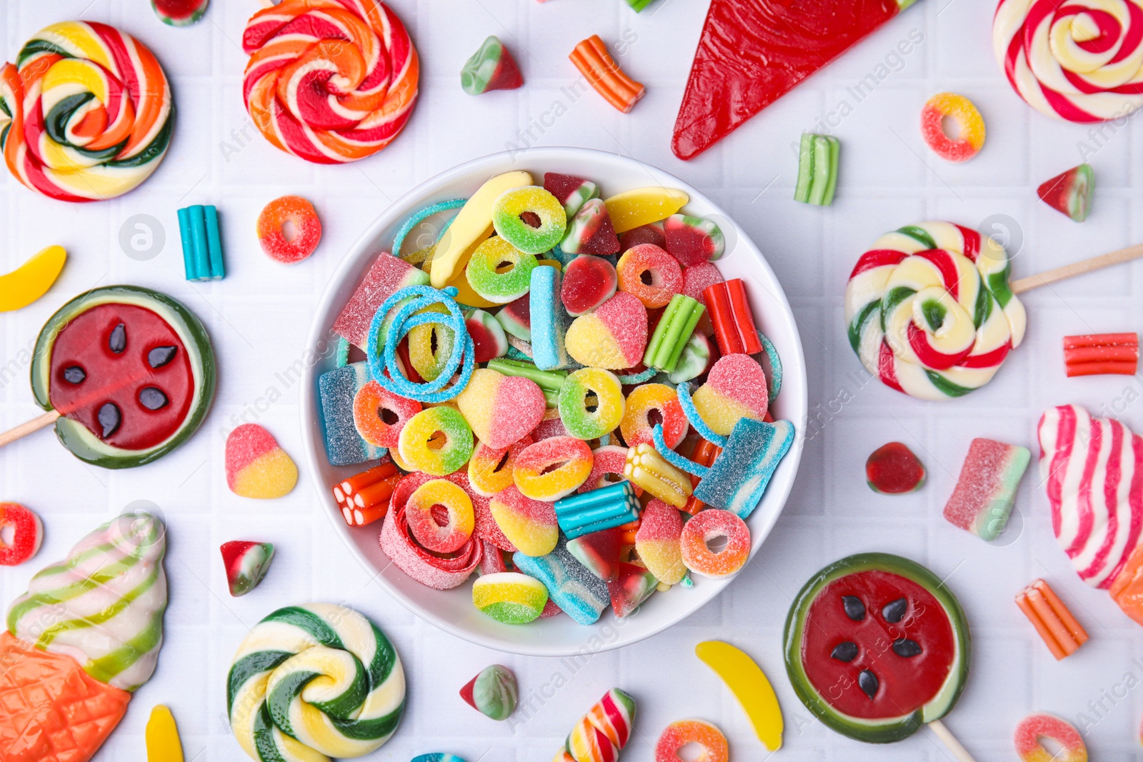 Photo of Many tasty colorful jelly candies and lollipops on white tiled table, flat lay