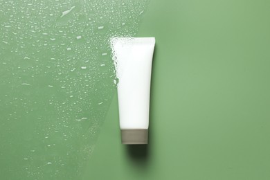 Tube with moisturizing cream on wet green surface, top view