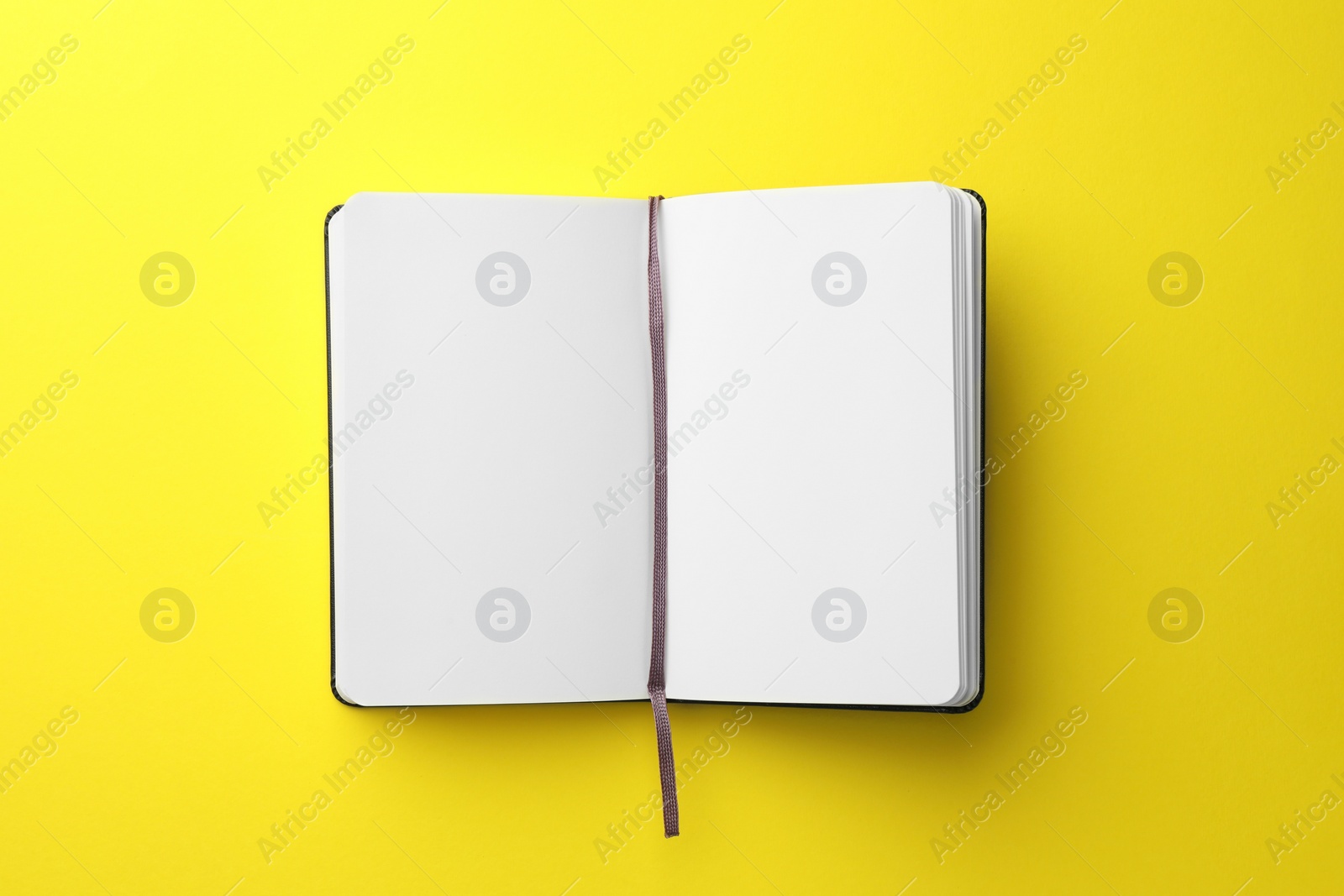 Photo of Open notebook with blank pages on yellow background, top view. Space for text