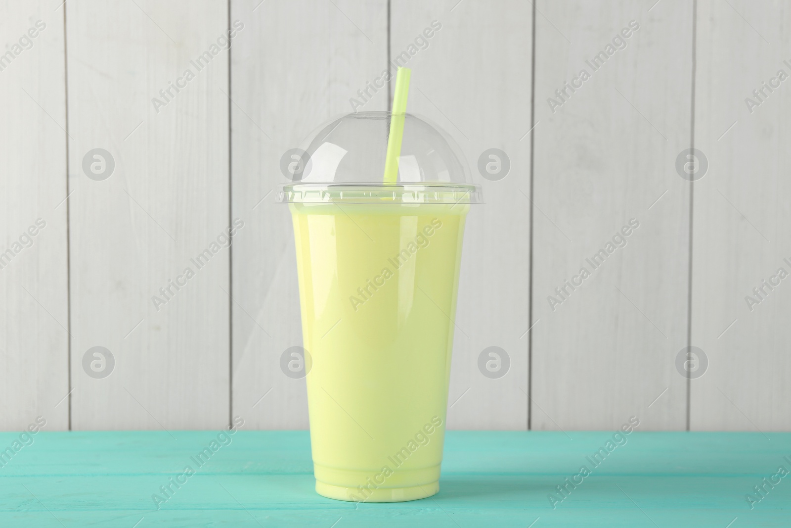 Photo of Tasty smoothie in plastic cup on light blue table against white wooden wall