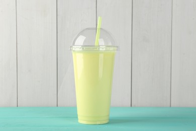 Photo of Tasty smoothie in plastic cup on light blue table against white wooden wall