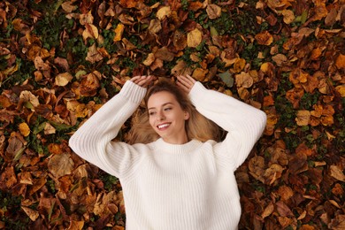 Smiling woman lying among autumn leaves outdoors, top view