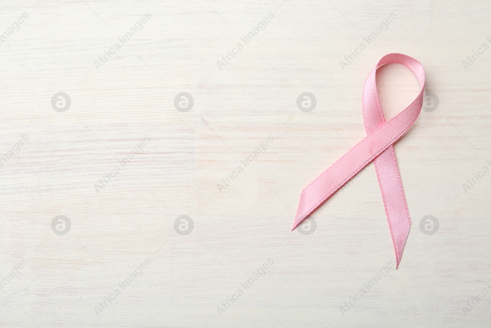 Photo of Pink awareness ribbon on light wooden table, top view. Space for text