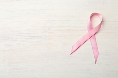 Pink awareness ribbon on light wooden table, top view. Space for text