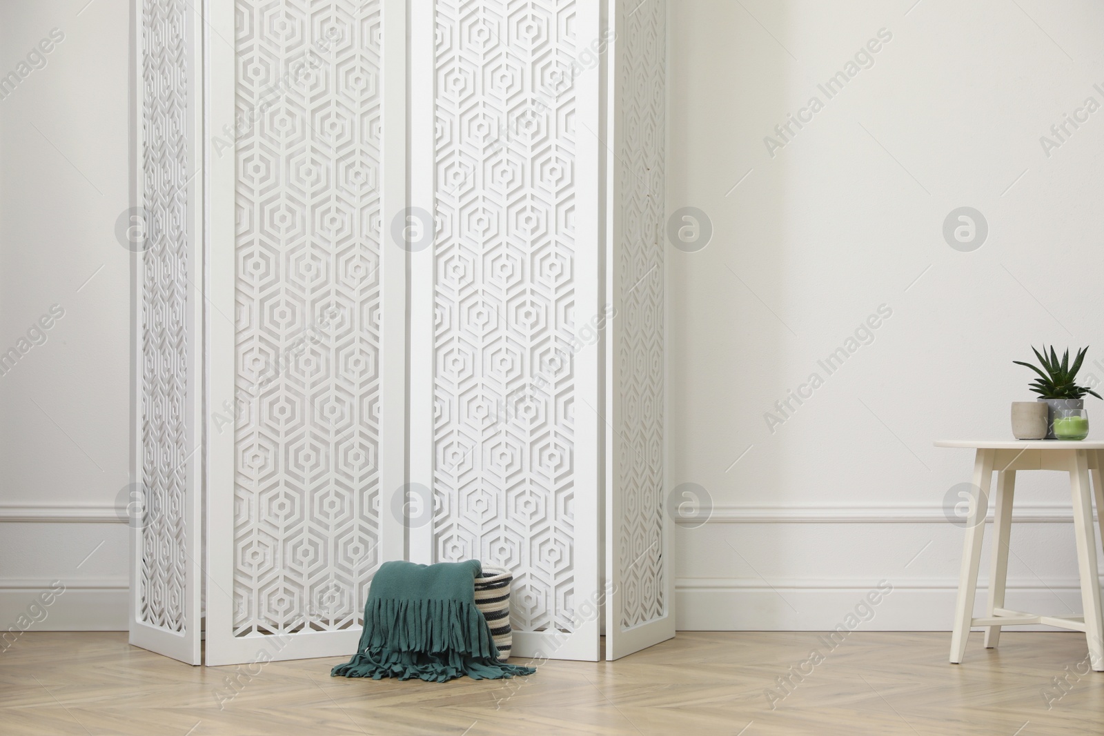 Photo of Folding screen and small table with houseplants near white wall in room. Interior design