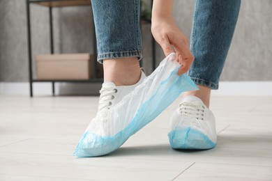 Woman wearing blue shoe covers onto her sneakers indoors, closeup