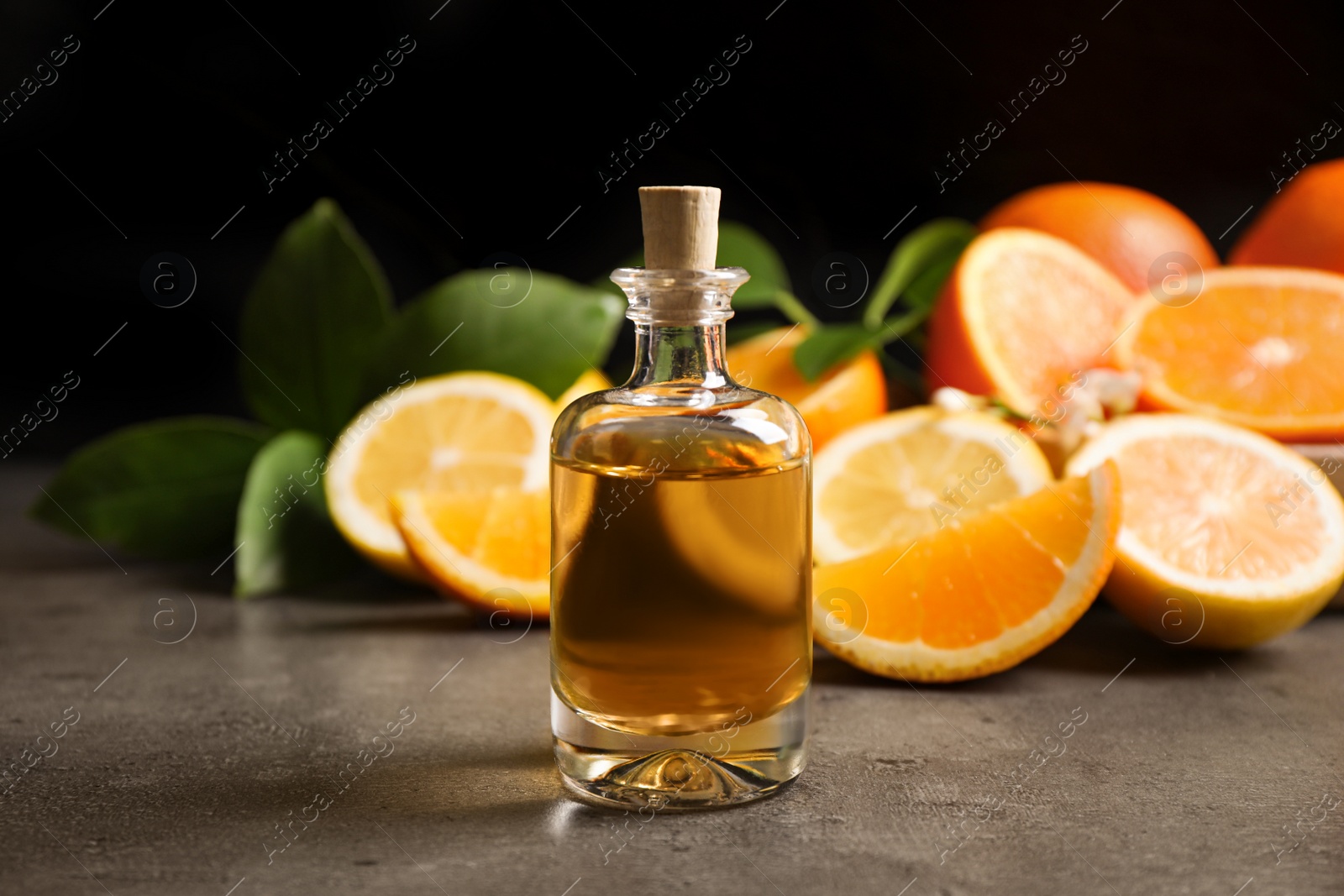 Photo of Bottle of essential oil and citrus fruits on grey table