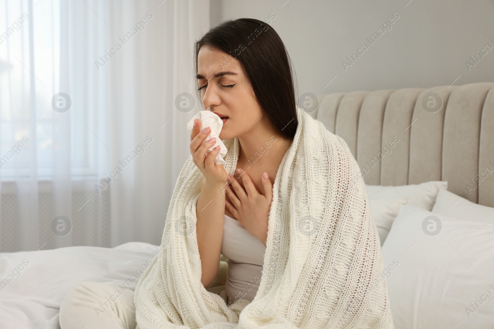 Photo of Sick young woman with tissue wrapped in knitted plaid at home