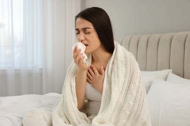 Sick young woman with tissue wrapped in knitted plaid at home