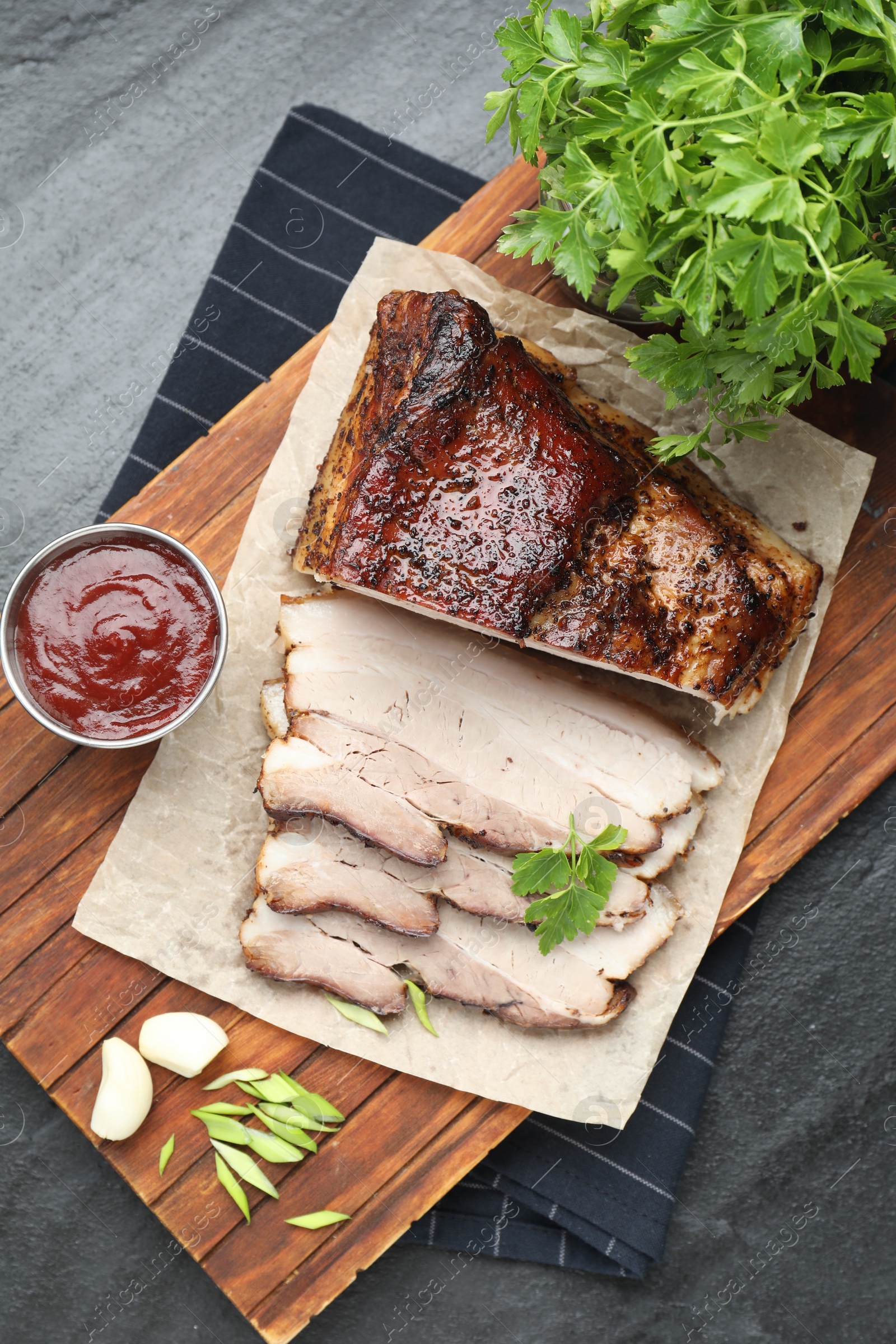 Photo of Pieces of baked pork belly served with sauce and parsley on black textured table, top view