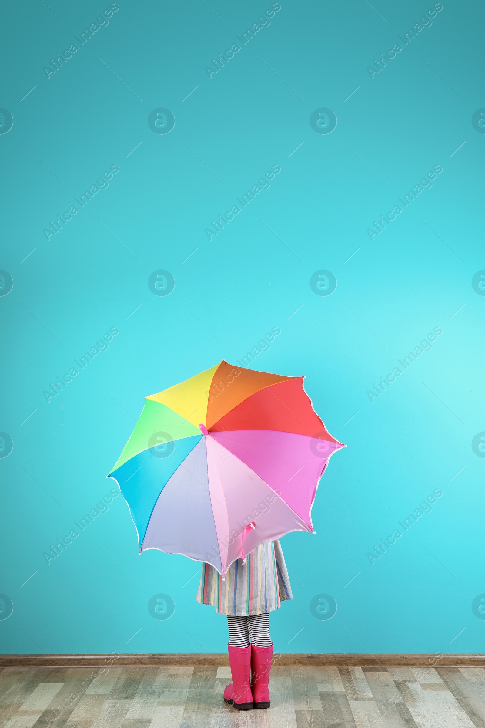 Photo of Little girl with rainbow umbrella near color wall. Space for text