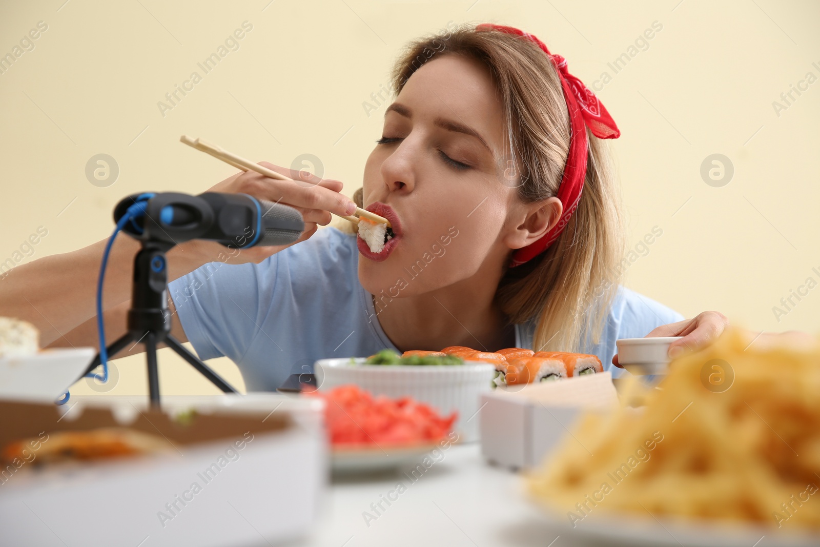 Photo of Food blogger eating in front of microphone at table against light background. Mukbang vlog