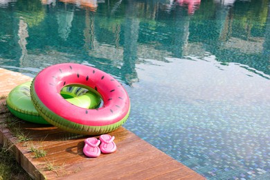 Photo of Inflatable rings and flip flops on wooden deck near swimming pool. Luxury resort