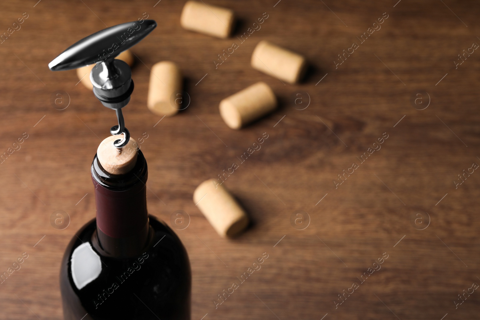 Photo of Opening wine bottle with corkscrew on wooden table, closeup. Space for text