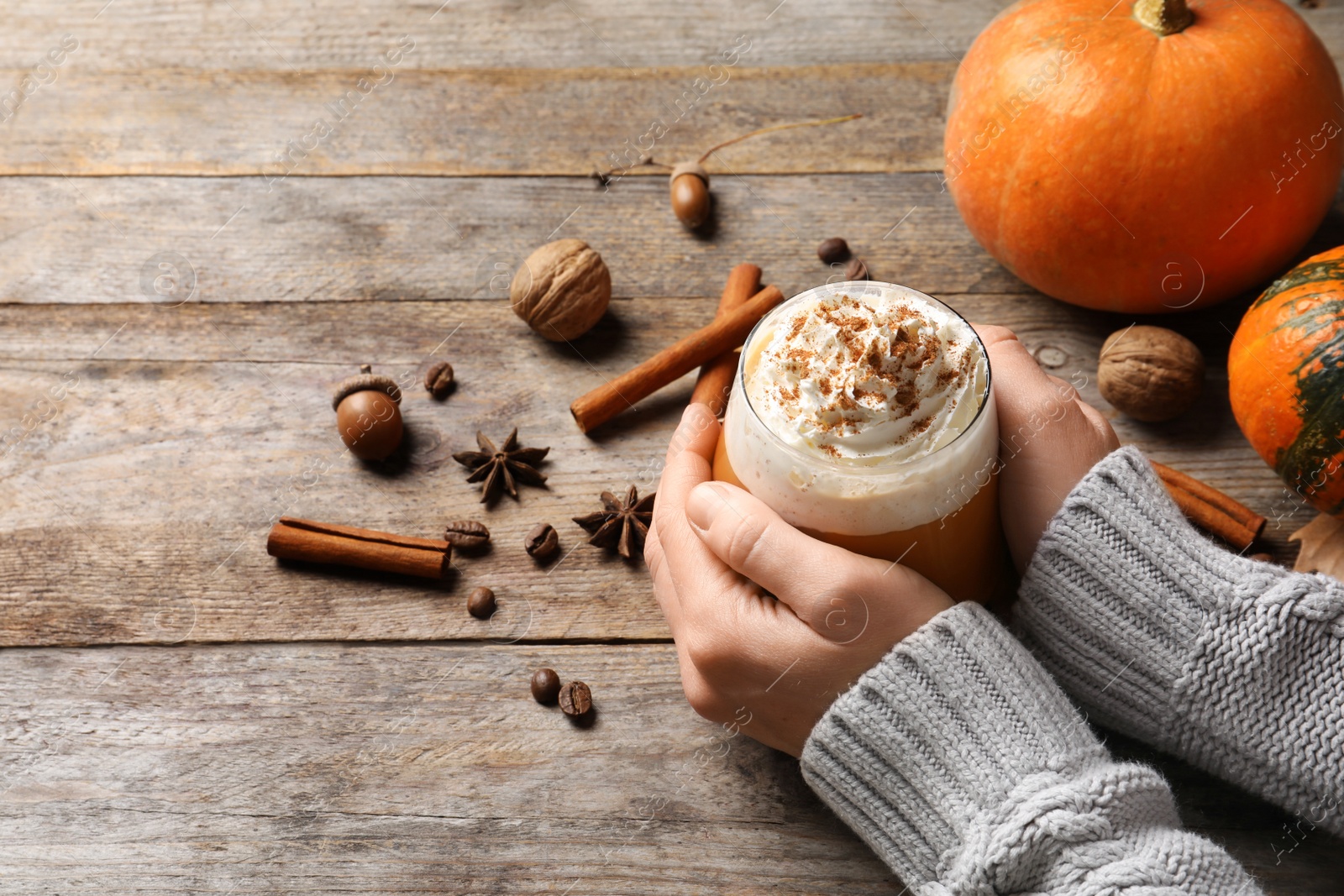 Photo of Woman holding glass of tasty pumpkin spice latte on wooden table, closeup with space for text