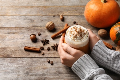 Photo of Woman holding glass of tasty pumpkin spice latte on wooden table, closeup with space for text