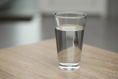 Glass of pure water on wooden table against blurred background, space for text