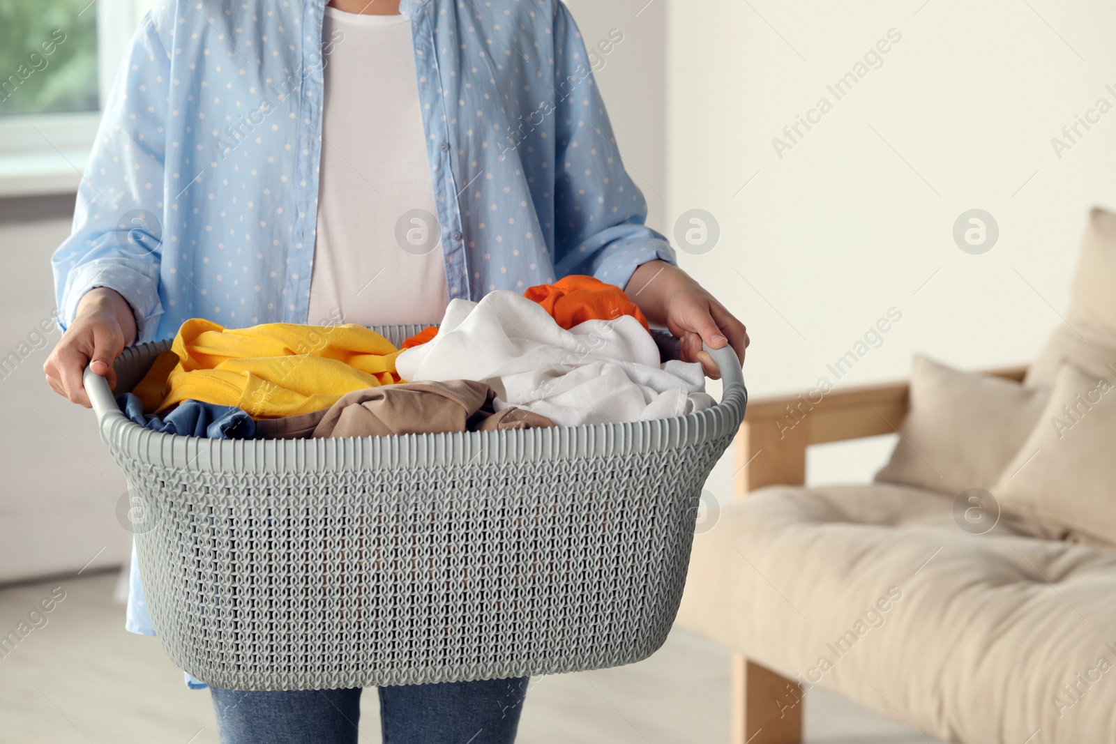 Photo of Woman with basket full of clean laundry indoors, closeup