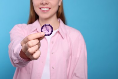 Photo of Woman holding condom on turquoise background, closeup. Safe sex
