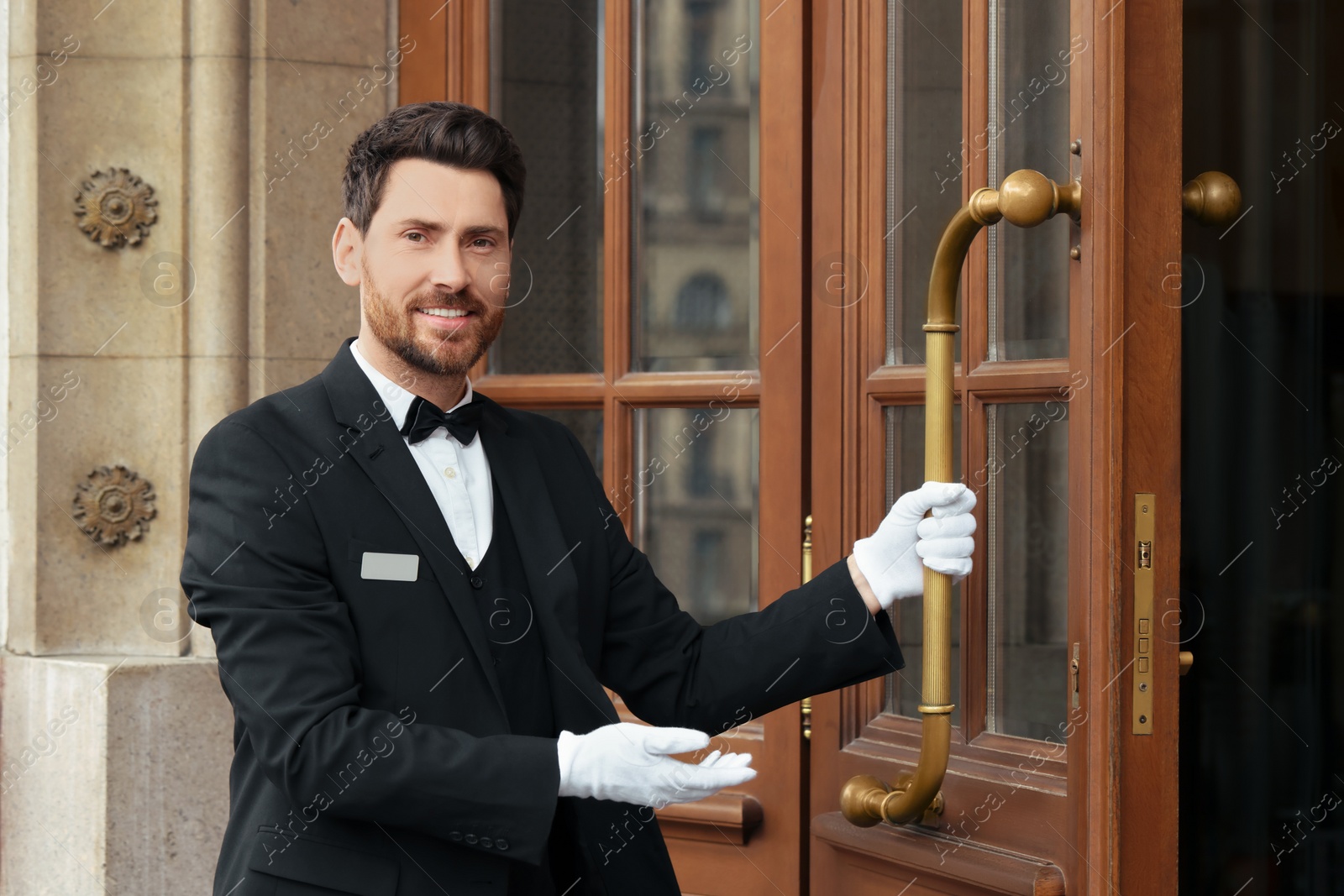 Photo of Butler in elegant suit and white gloves opening wooden hotel door