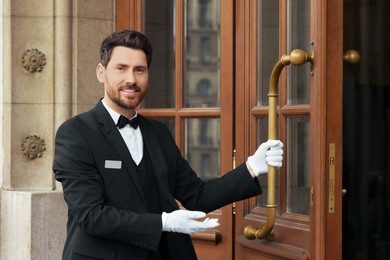 Butler in elegant suit and white gloves opening wooden hotel door