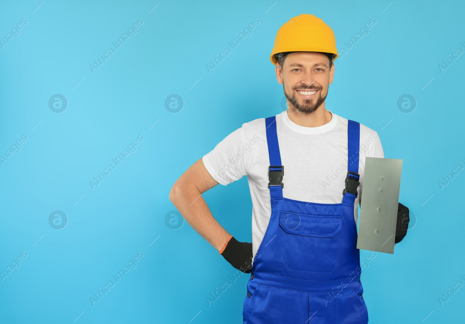 Photo of Professional worker in hard hat with putty knife on light blue background, space for text