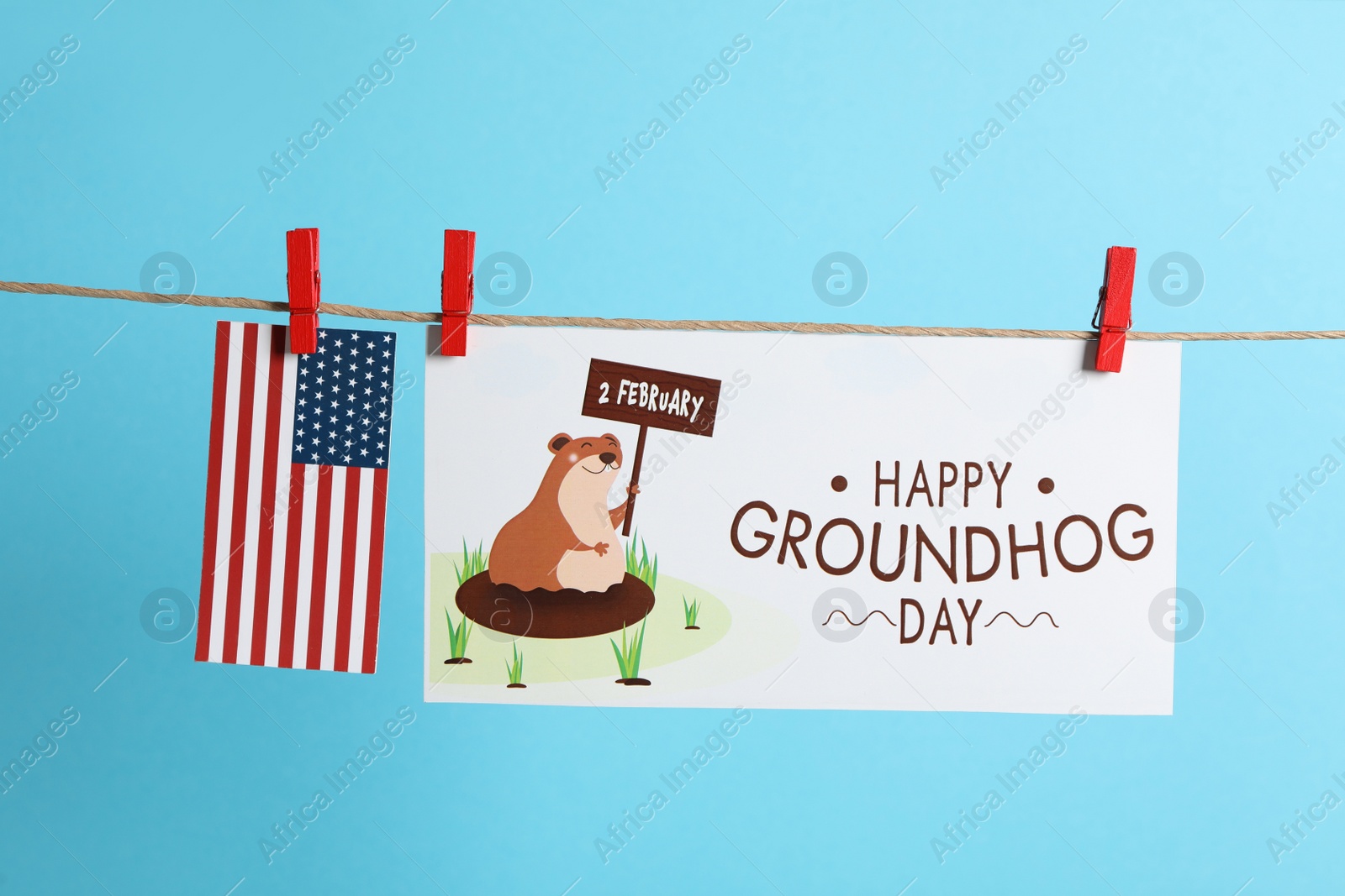 Photo of Happy Groundhog Day greeting card and American flag hanging on light blue background