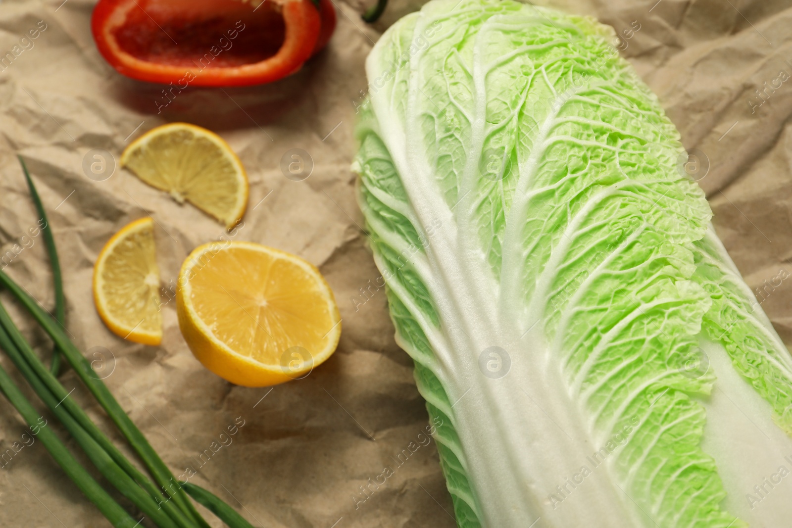 Photo of Fresh Chinese cabbage, lemon and green onion on kraft paper, closeup