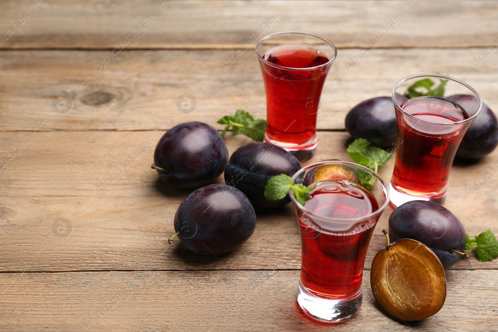 Photo of Delicious plum liquor, mint and ripe fruits on wooden table. Homemade strong alcoholic beverage