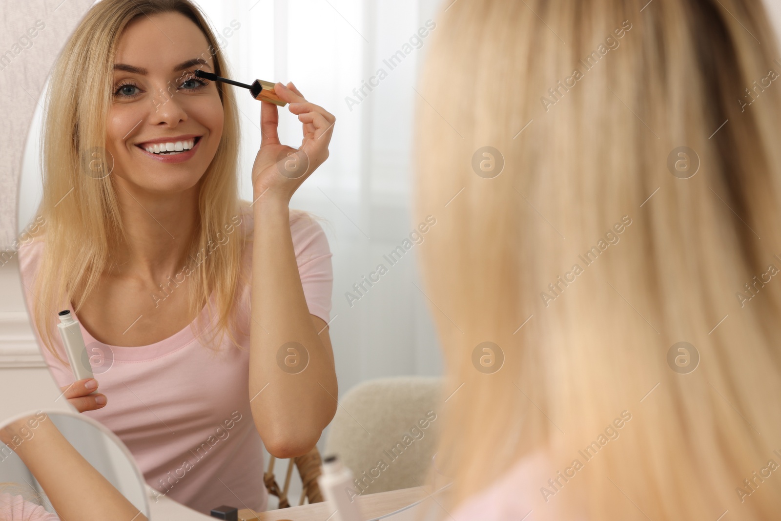 Photo of Beautiful woman applying mascara near mirror at home