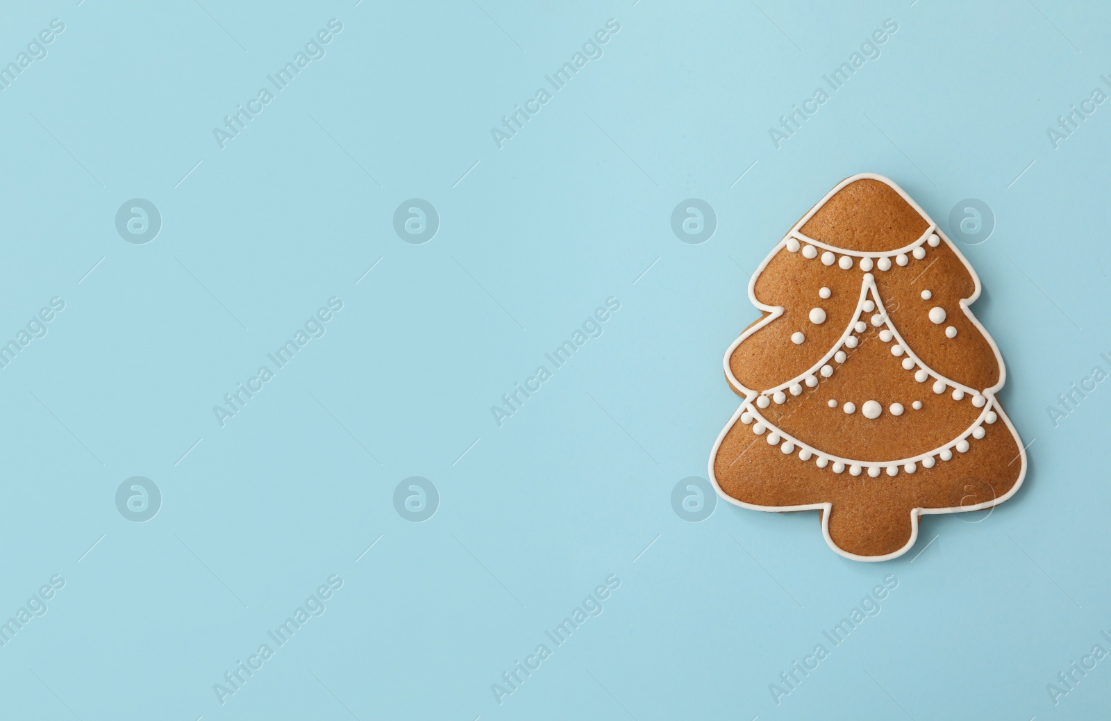 Photo of Christmas tree shaped gingerbread cookie on light blue background, top view. Space for text