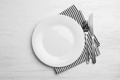 Photo of Empty plate, cutlery and napkin on white wooden background, flat lay