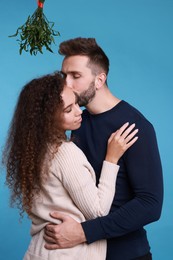 Lovely couple under mistletoe bunch on light blue background