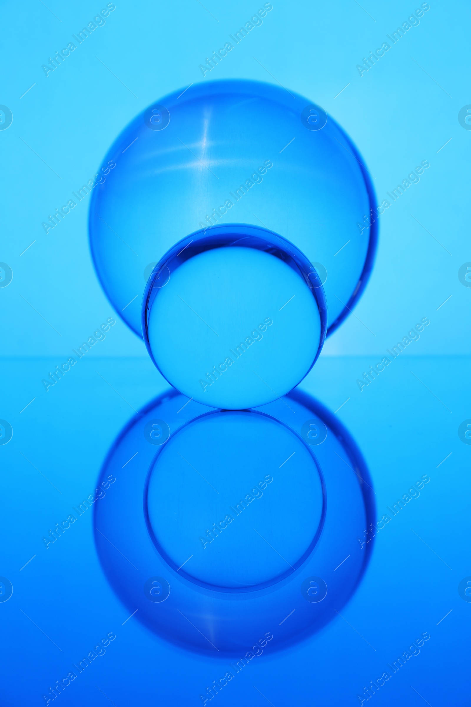 Photo of Transparent glass balls on mirror surface against blue background