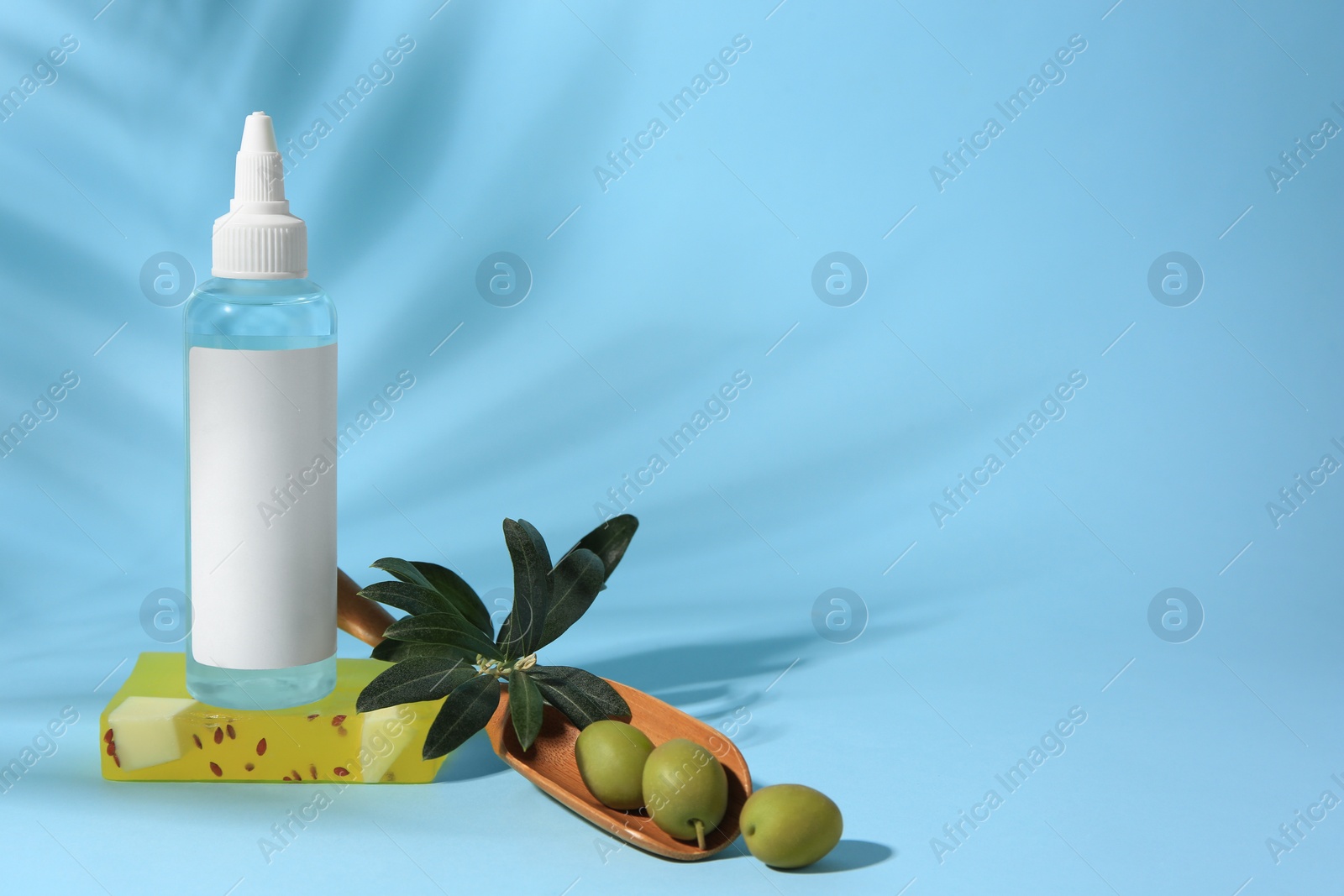 Photo of Bottle of cosmetic product, soap bar and olives on light blue background, space for text