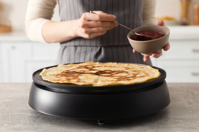 Photo of Woman cooking delicious crepe on electric pancake maker in kitchen, closeup