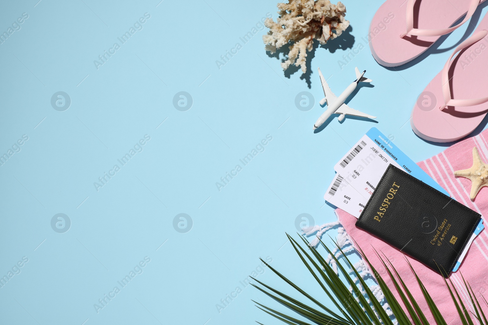 Photo of Passport with tickets, airplane model, flip flops, blanket, coral and palm leaf on light blue background, flat lay. Space for text