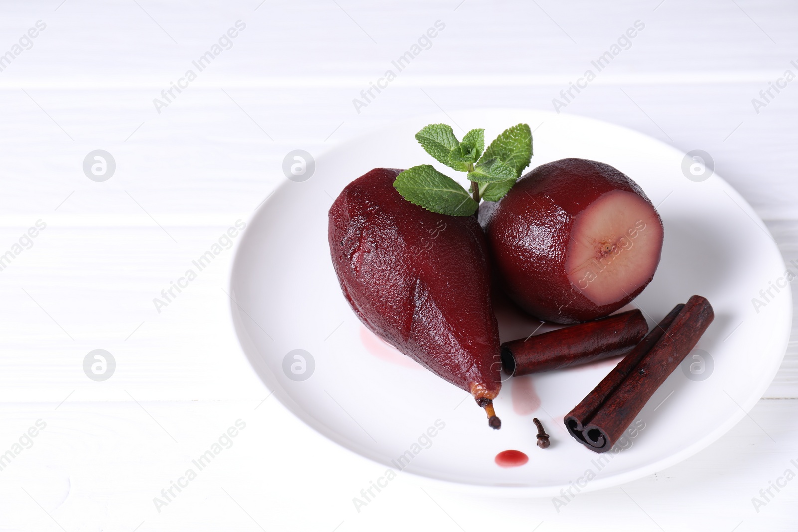 Photo of Tasty red wine poached pears with mint and cinnamon on white wooden table, closeup. Space for text
