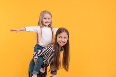 Portrait of cute little sisters on orange background, space for text
